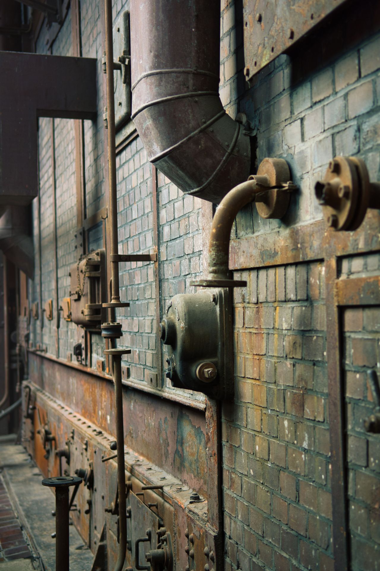 Metal pipes and bolted flanges running along the wall of an industrial plant.